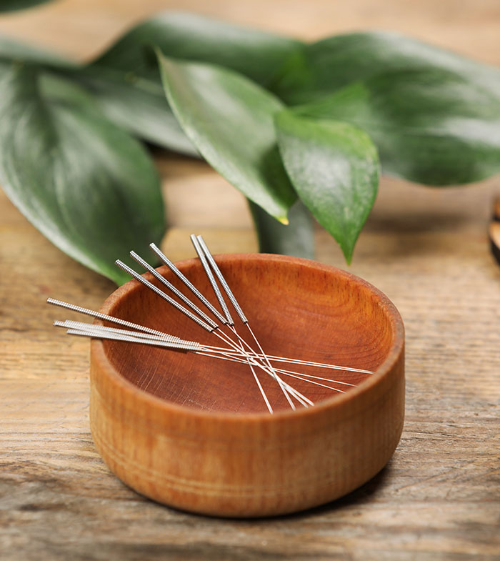 Bowl with acupuncture needles on wooden table