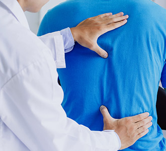 Physical therapist treating young man's back as part of chiropractic care regime at Summit Health Group